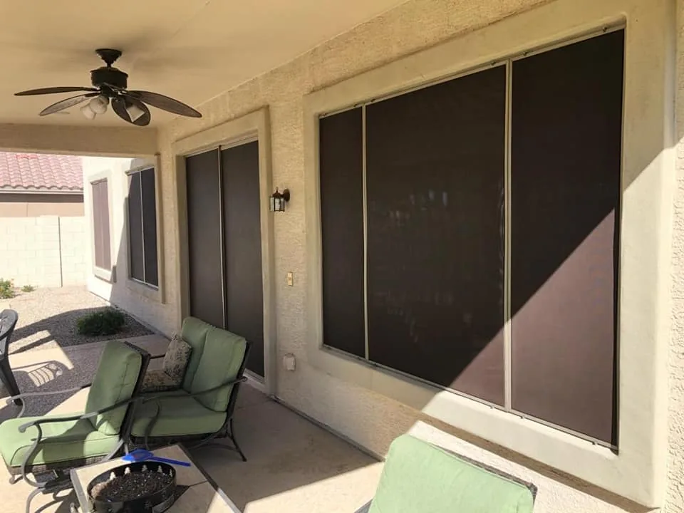 Covered patio with black retractable screens on large windows and green patio chairs.
