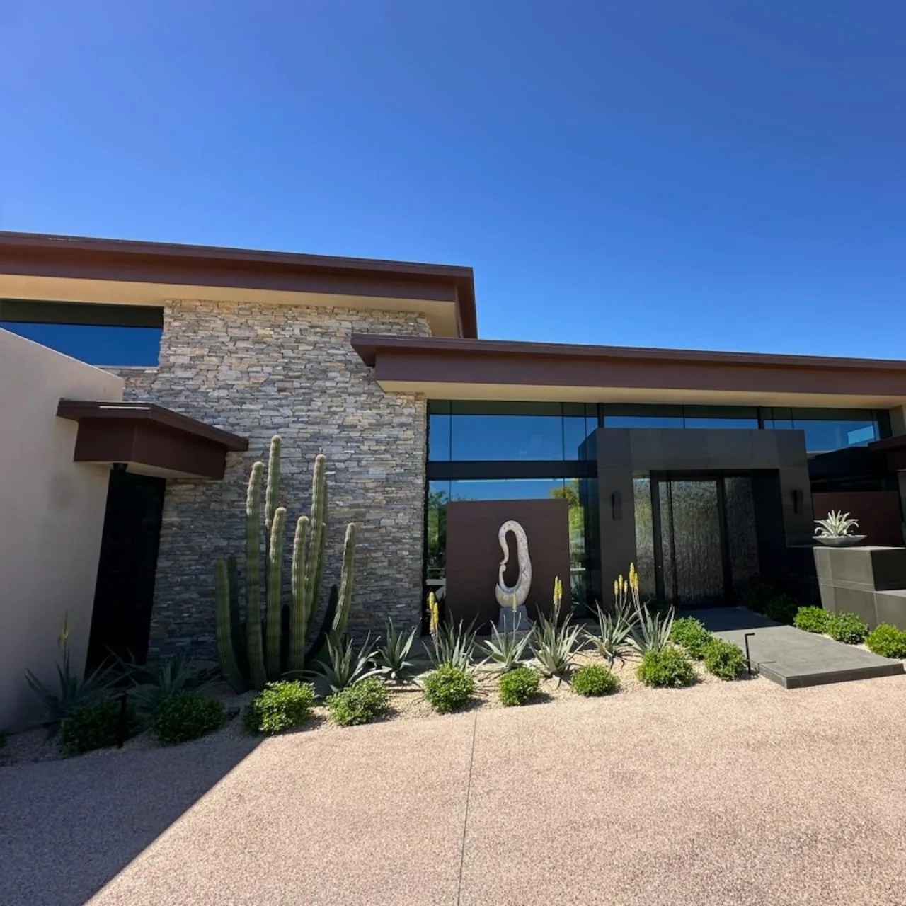 Modern desert home exterior with stone accent wall, large windows, and desert landscaping.