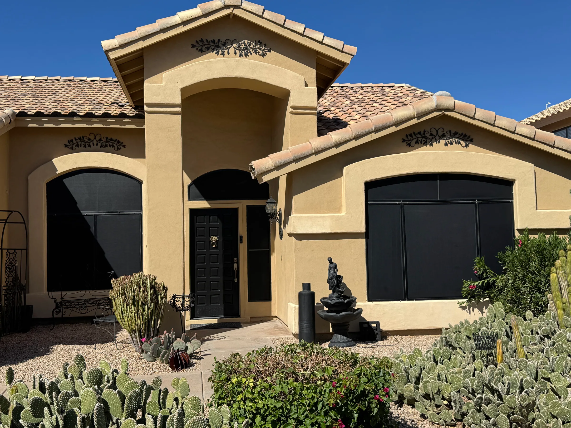 Tan stucco home with black garage doors and arched entryway surrounded by desert landscaping.
