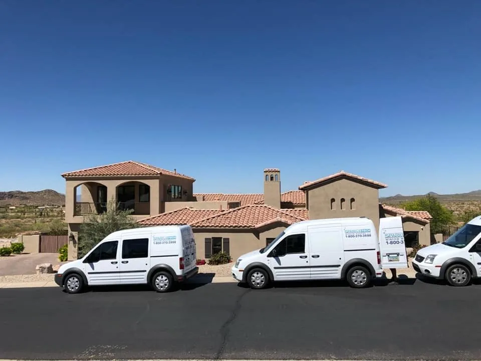 Three white service vans parked in front of a Southwestern-style home in a desert setting.