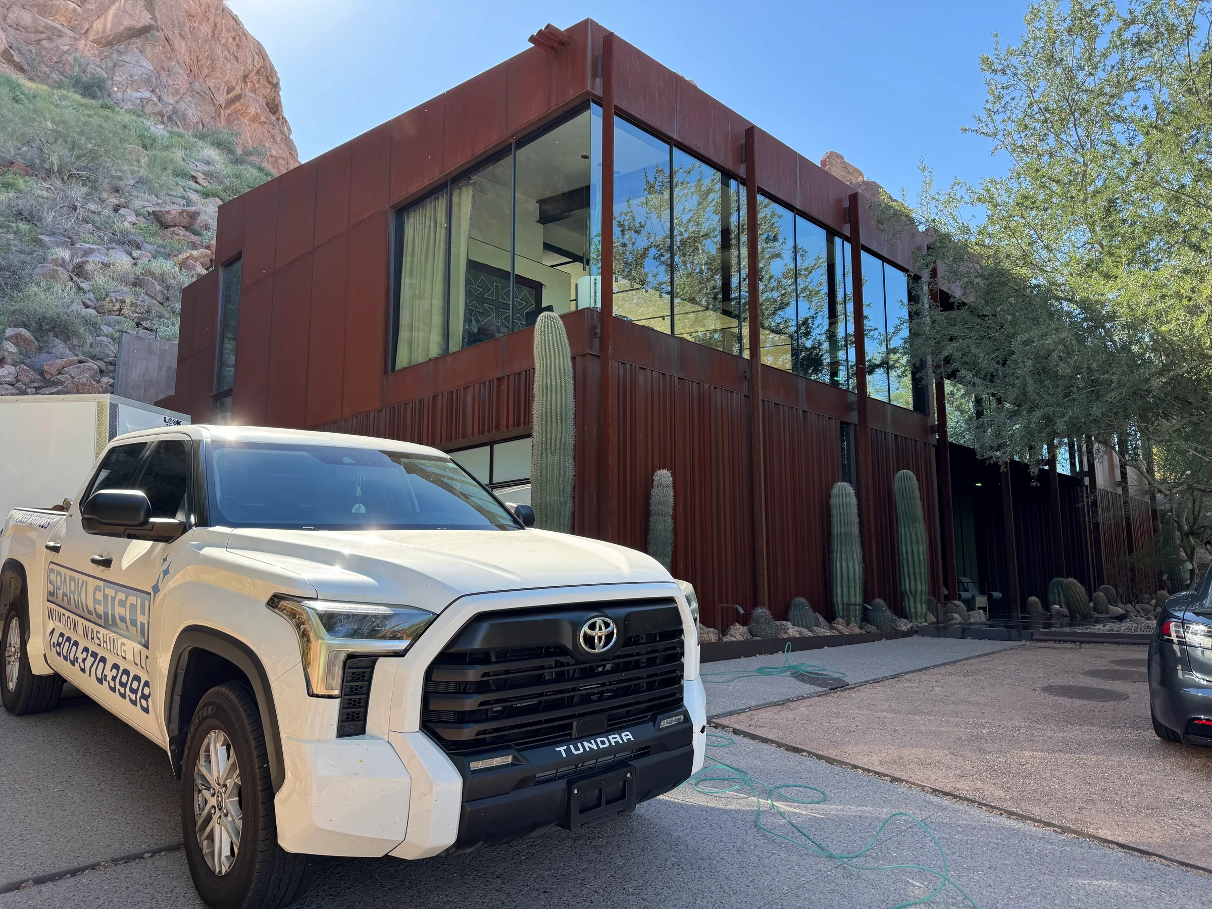 White Toyota Tundra pickup truck with Sparkle Tech Screen Service branding parked in front of modern rust-colored building wi